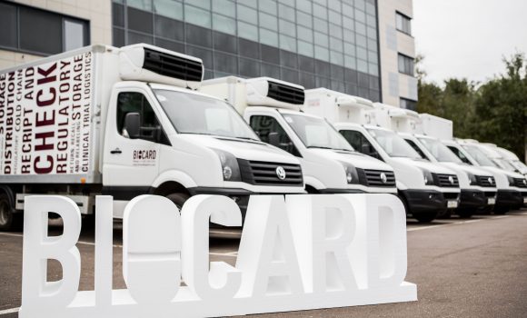 Логотип Biocard на фоне грузовиков, готовящихся к автомобильной грузоперевозке температурных и сборных грузов